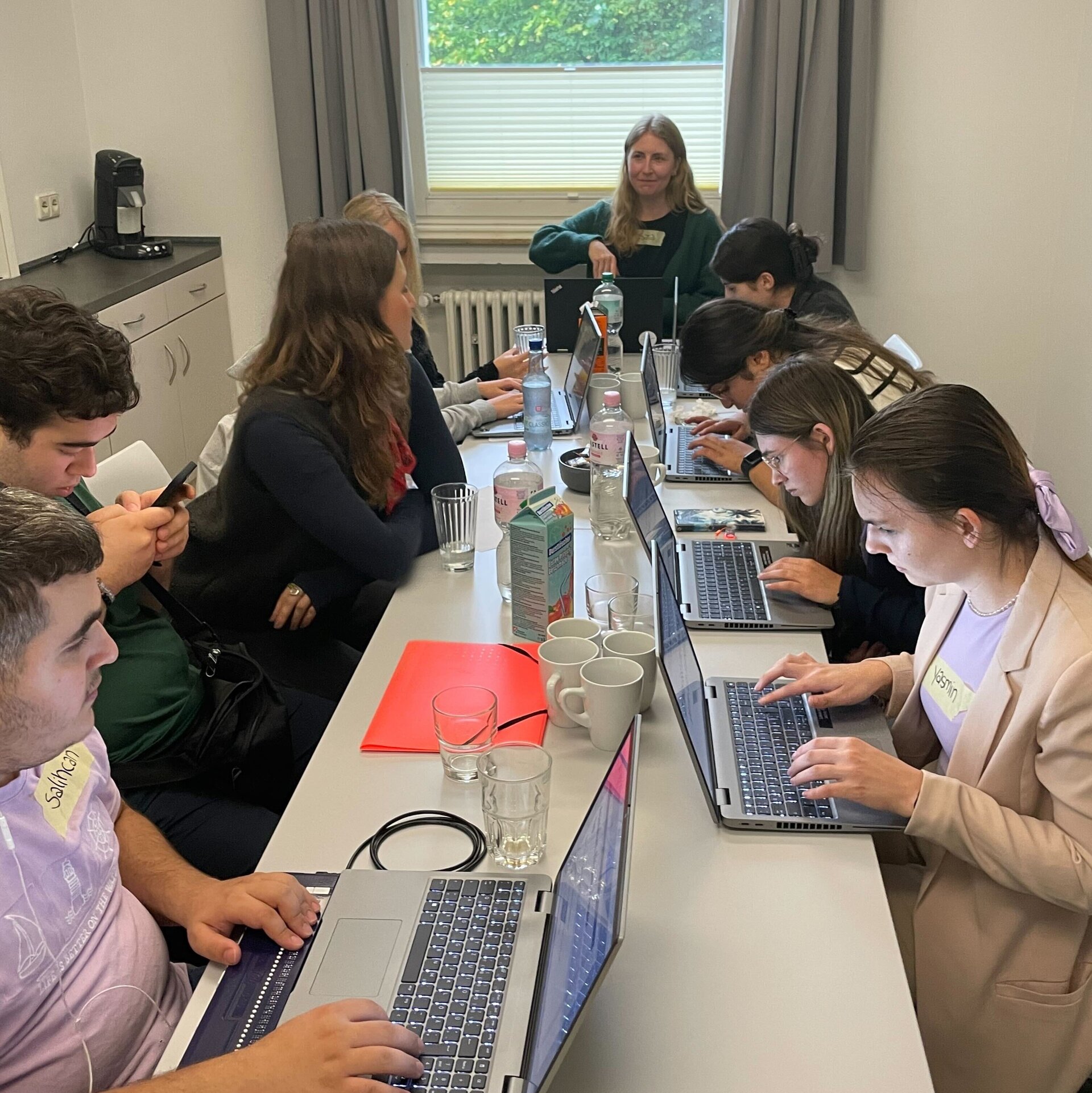 Verschiedene Menschen sitzen an einem Tisch und arbeiten an Laptops.